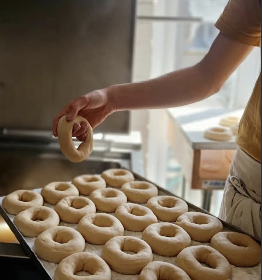 2 cooks laying rings of bagel dough onto a baking tray