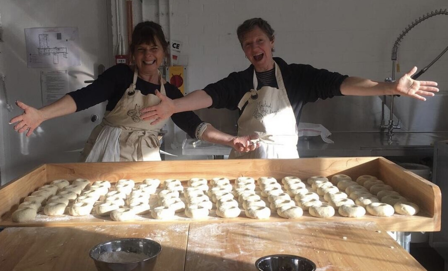 2 trays of freshly baked bagels covered in poppy and sesame seeds sitting in front of jars of cooking ingredidents