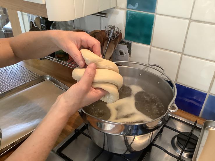 Rings of bagel dough going into a pot of boiling water on a stove